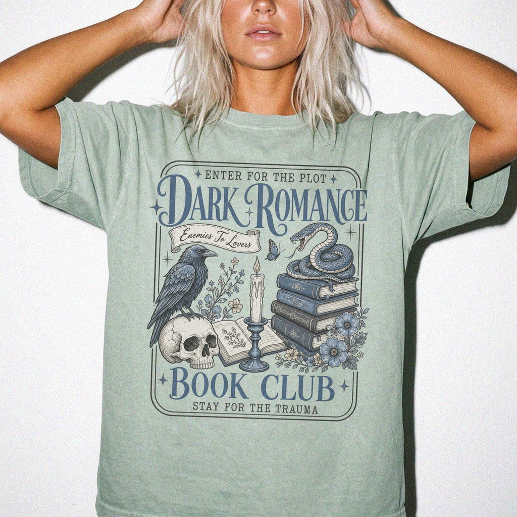 Bay color Comfort Colors 1717 relaxed fit t-shirt with gothic dark romance graphic — a raven perched on a skull, a snake coiled on stacked books, a candle, and florals, with the text "Dark Romance Book Club — Enter for the Plot, Stay for the Trauma"