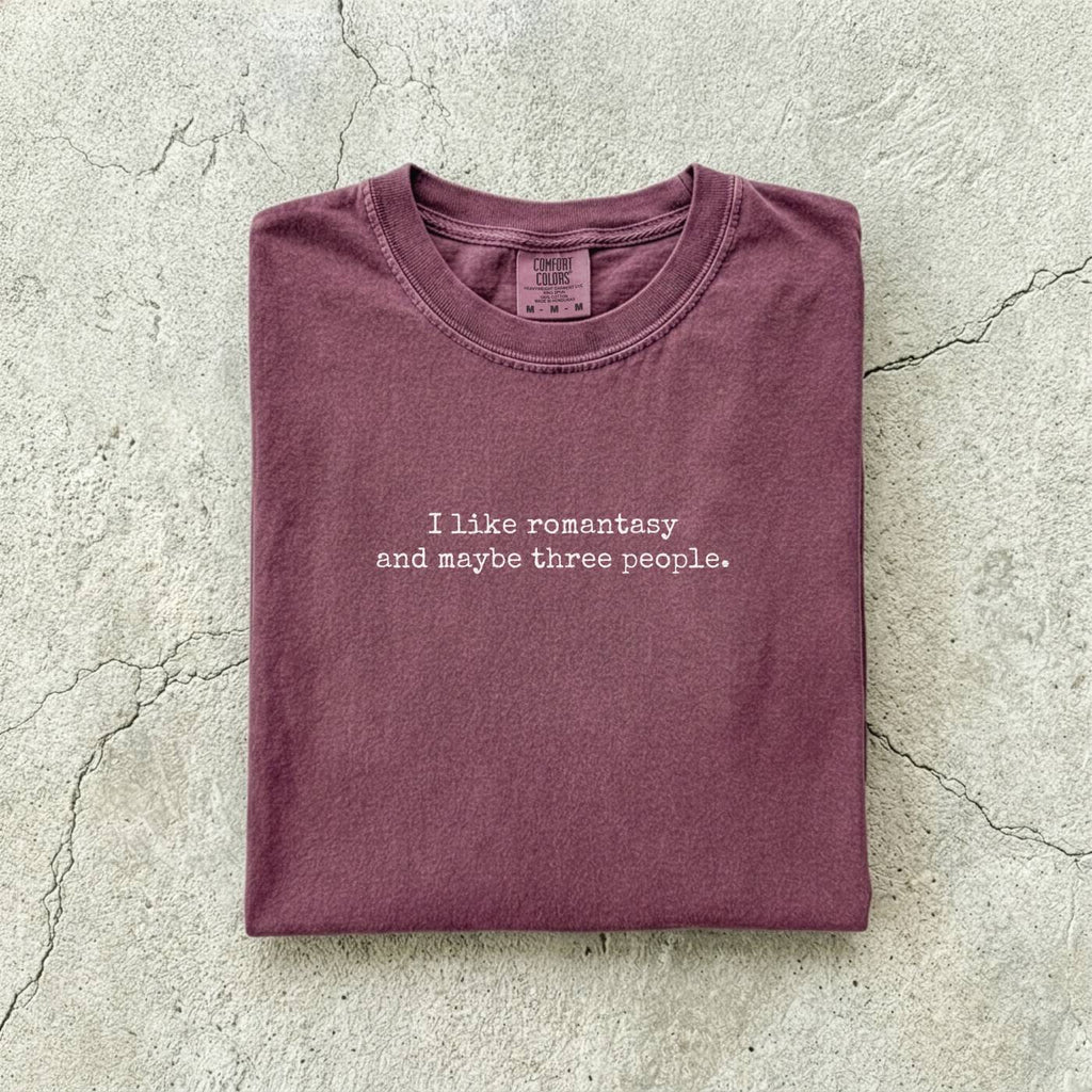 Berry Comfort Colors tee folded flat reading "I like romantasy and maybe three people." in a typewriter font.