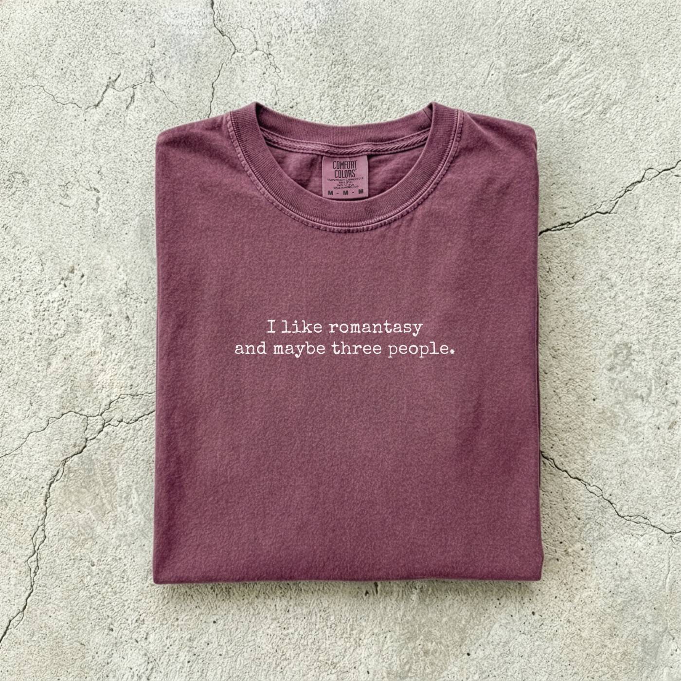 Berry Comfort Colors tee folded flat reading "I like romantasy and maybe three people." in a typewriter font.