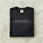 Black Comfort Colors tee folded flat on a concrete background reading "Morally grey readers club. We prefer our men written by women." in a minimal typewriter font.
