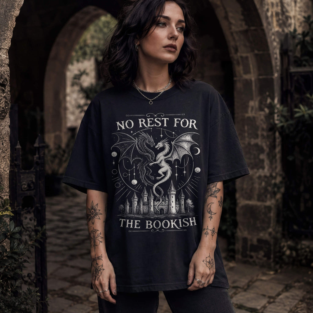 Black color Comfort Colors 1717 relaxed fit t-shirt with gothic romantasy graphic — two dragons soaring over a castle beneath moons and celestial details, with the text "No Rest for the Bookish"