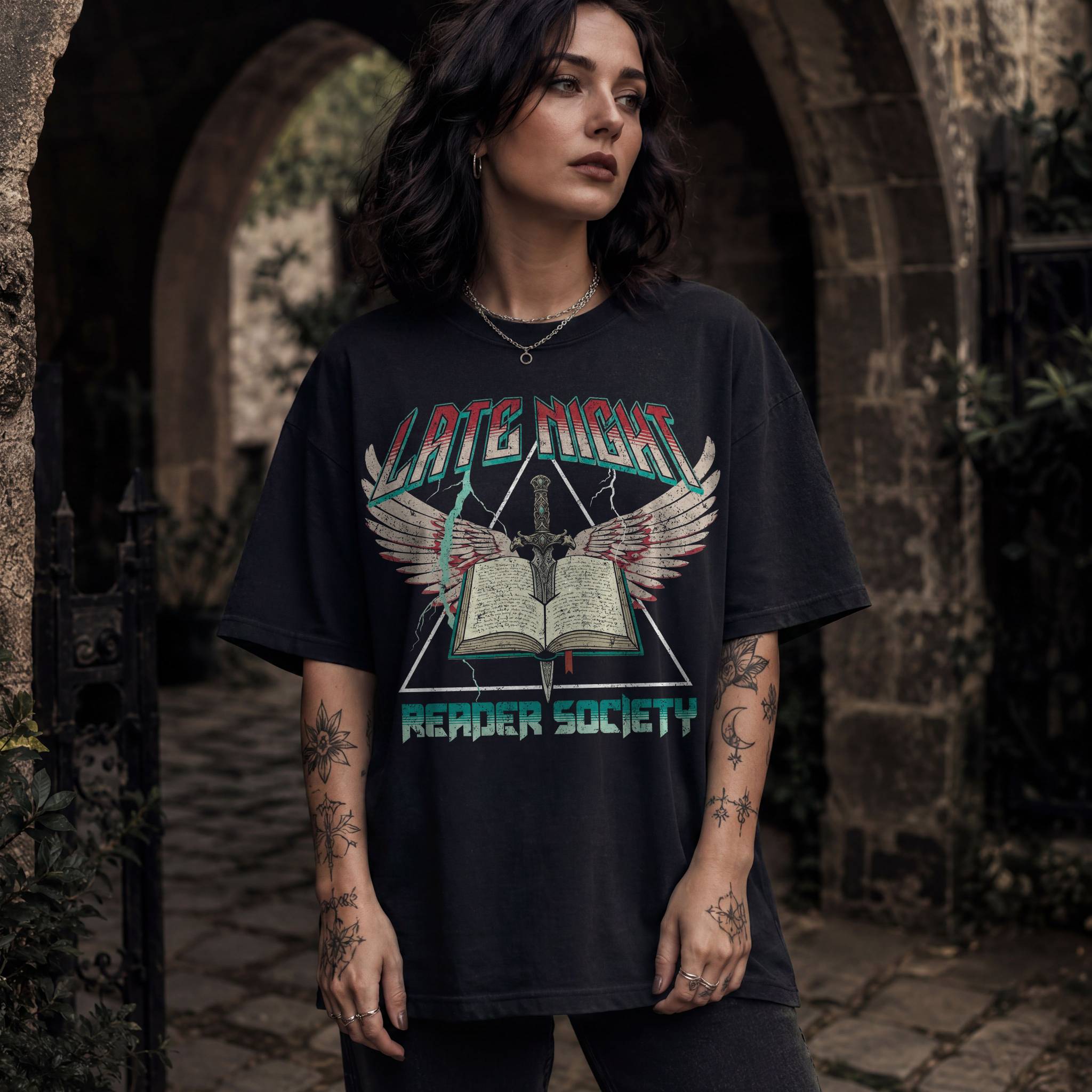 Woman wearing black Comfort Colors relaxed tee with Late Night Reader Society vintage metal graphic — winged open book and dagger design