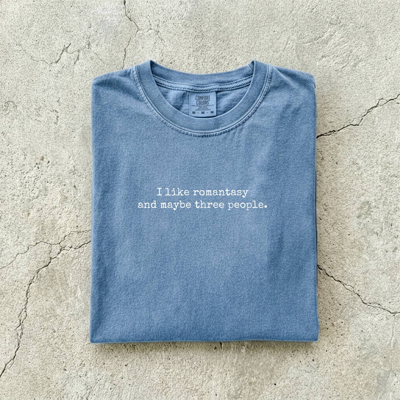 Blue Jean Comfort Colors tee folded flat reading "I like romantasy and maybe three people." in a typewriter font.