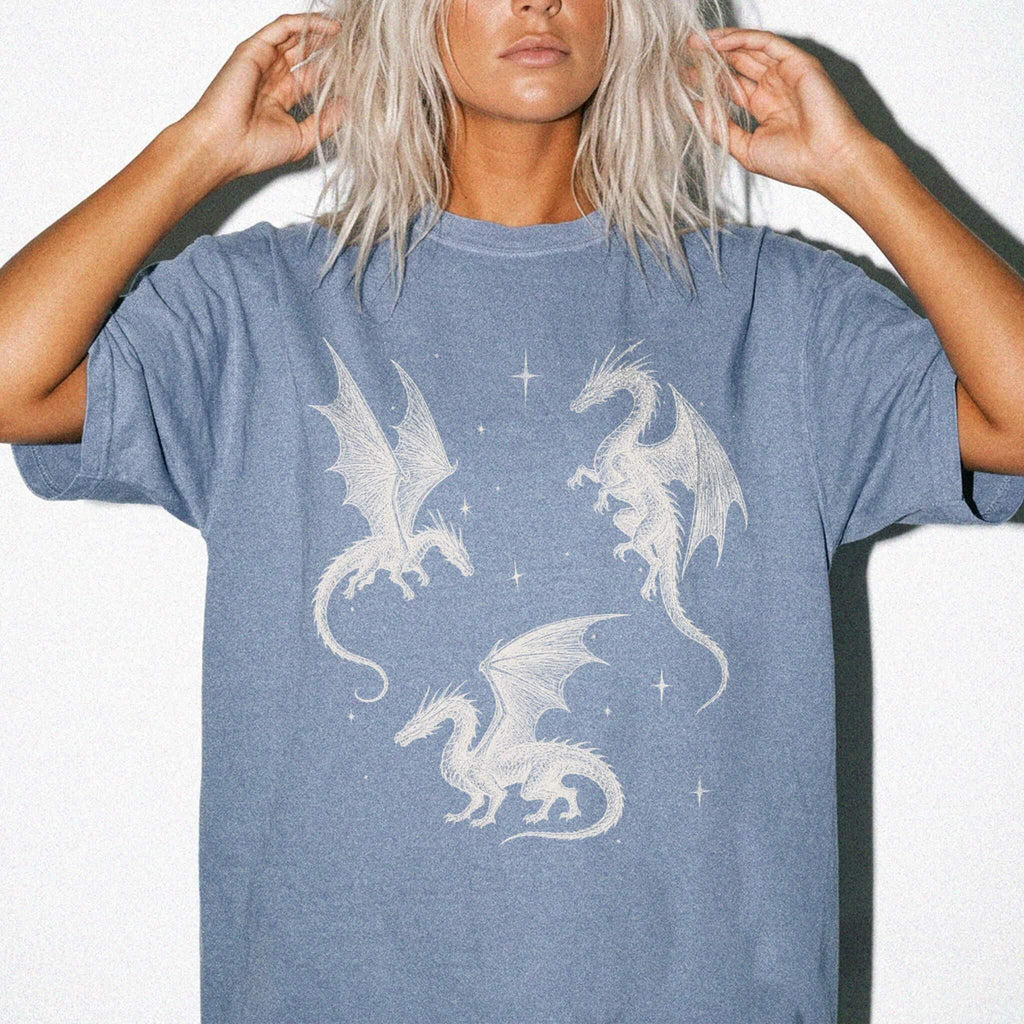 Blue Jean color Comfort Colors 1717 relaxed fit t-shirt with whimsigoth fantasy graphic — three detailed dragon illustrations surrounded by stars and celestial details in off-white line art