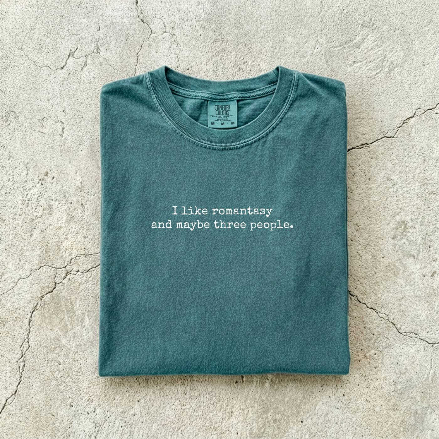 Blue Spruce Comfort Colors tee folded flat reading "I like romantasy and maybe three people." in a typewriter font.