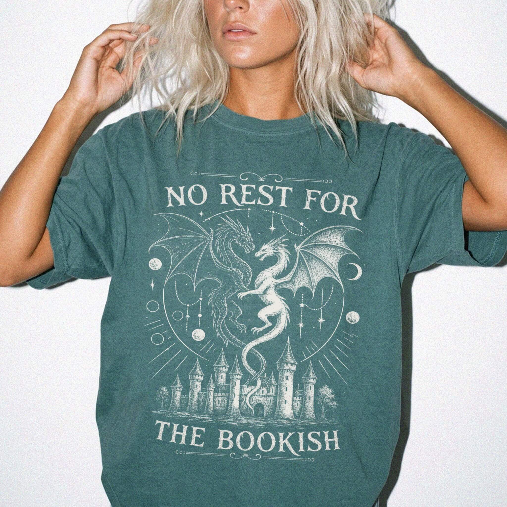 Blue Spruce Comfort Colors 1717 relaxed fit t-shirt with gothic romantasy graphic — two dragons soaring over a castle beneath moons and celestial details, with the text "No Rest for the Bookish"