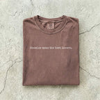 Espresso Comfort Colors tee folded flat on a concrete background reading "Enemies make the best lovers." in a minimal typewriter font.