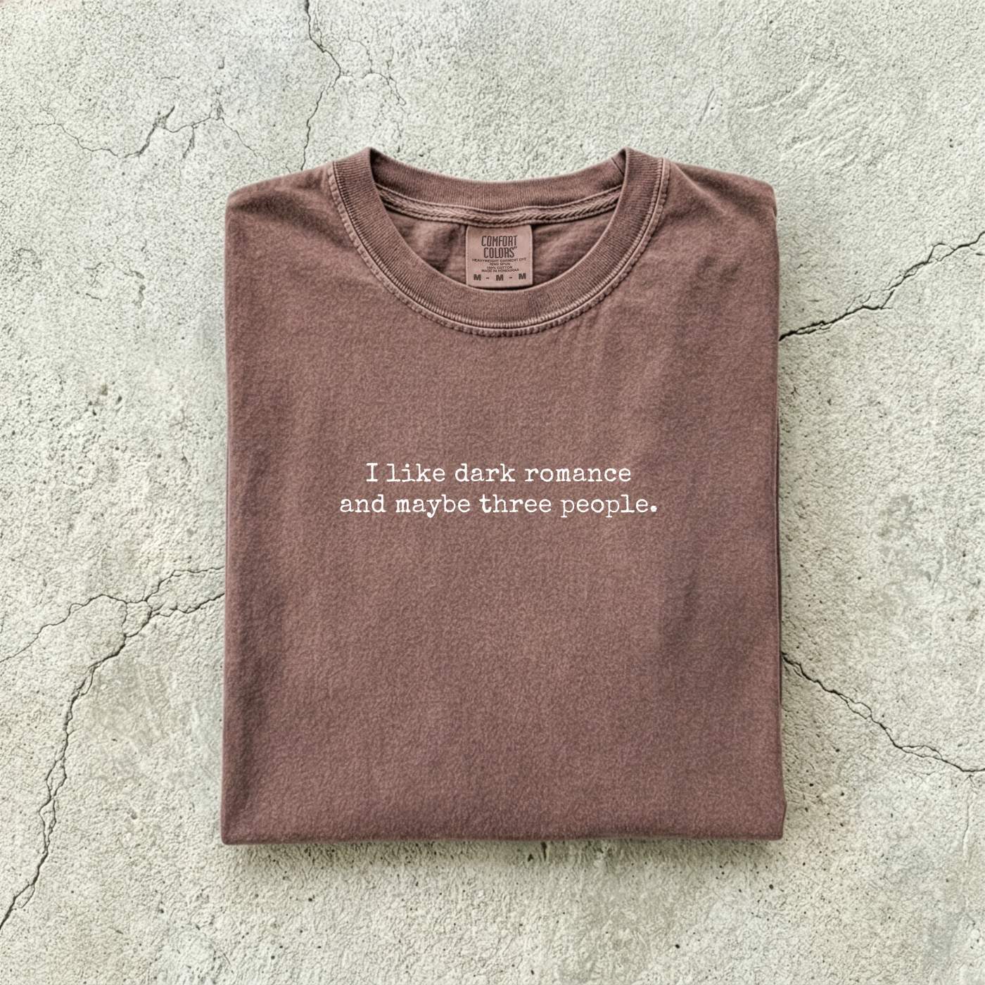 Espresso Comfort Colors tee folded flat reading "I like dark romance and maybe three people." in a minimalist typewriter font.
