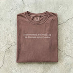 Espresso Comfort Colors tee folded flat on a concrete background reading "Introverted, but willing to discuss spicy books." in a minimal typewriter font.