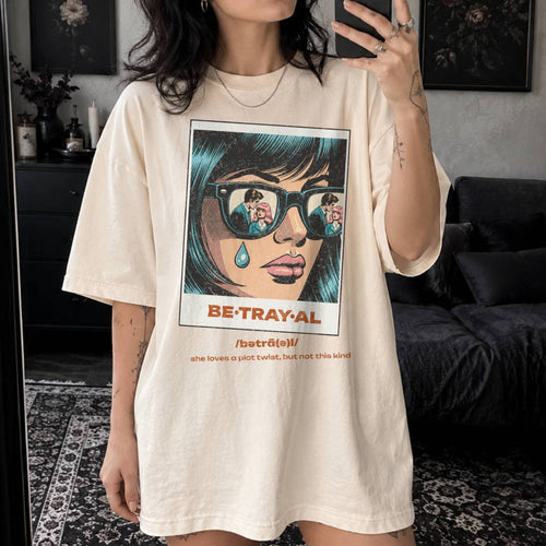 Ivory Comfort Colors 1717 relaxed fit t-shirt with retro pop art graphic — a woman with teal hair and sunglasses reflecting a couple, a single tear on her cheek, with the word BE·TRAY·AL (betrayal) and the tagline "she loves a plot twist, but not this kind" 