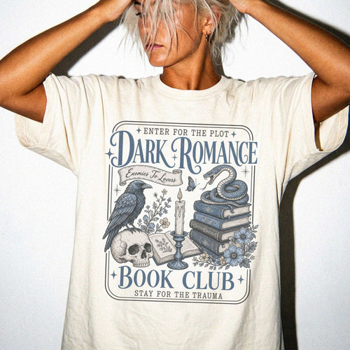 Ivory color Comfort Colors 1717 relaxed fit t-shirt with gothic dark romance graphic — a raven perched on a skull, a snake coiled on stacked books, a candle, and florals, with the text "Dark Romance Book Club — Enter for the Plot, Stay for the Trauma"