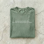 Moss Comfort Colors tee folded flat on a concrete background reading "Morally grey readers club. We prefer our men written by women." in a minimal typewriter font.