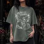 Woman wearing a moss color relaxed fit Comfort Colors tee with a vintage graphic of a woman warrior dragon rider and "We Ride at Dawn" text.