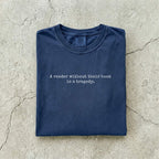 Navy Comfort Colors tee folded flat on a concrete background reading "A reader without their book is a tragedy." in a minimal typewriter font.