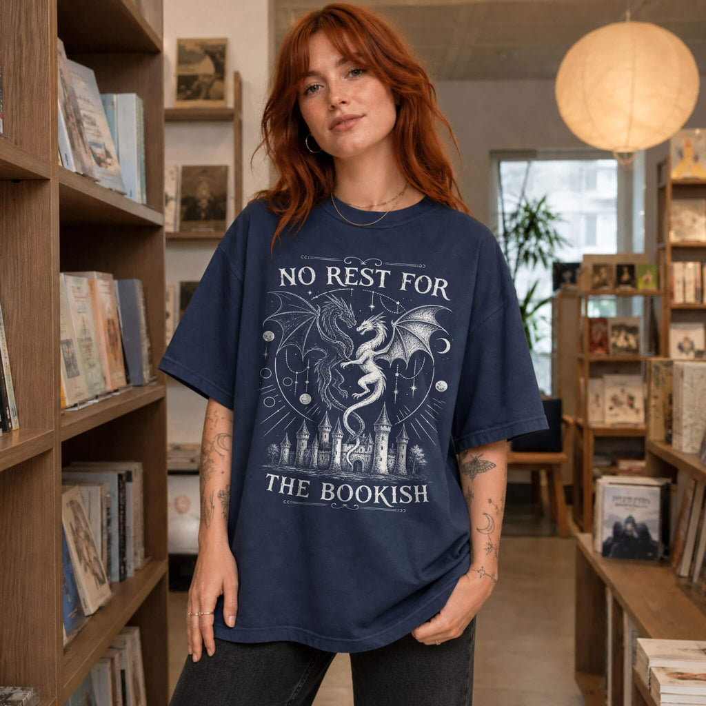 Navy color Comfort Colors 1717 relaxed fit t-shirt with gothic romantasy graphic — two dragons soaring over a castle beneath moons and celestial details, with the text "No Rest for the Bookish"