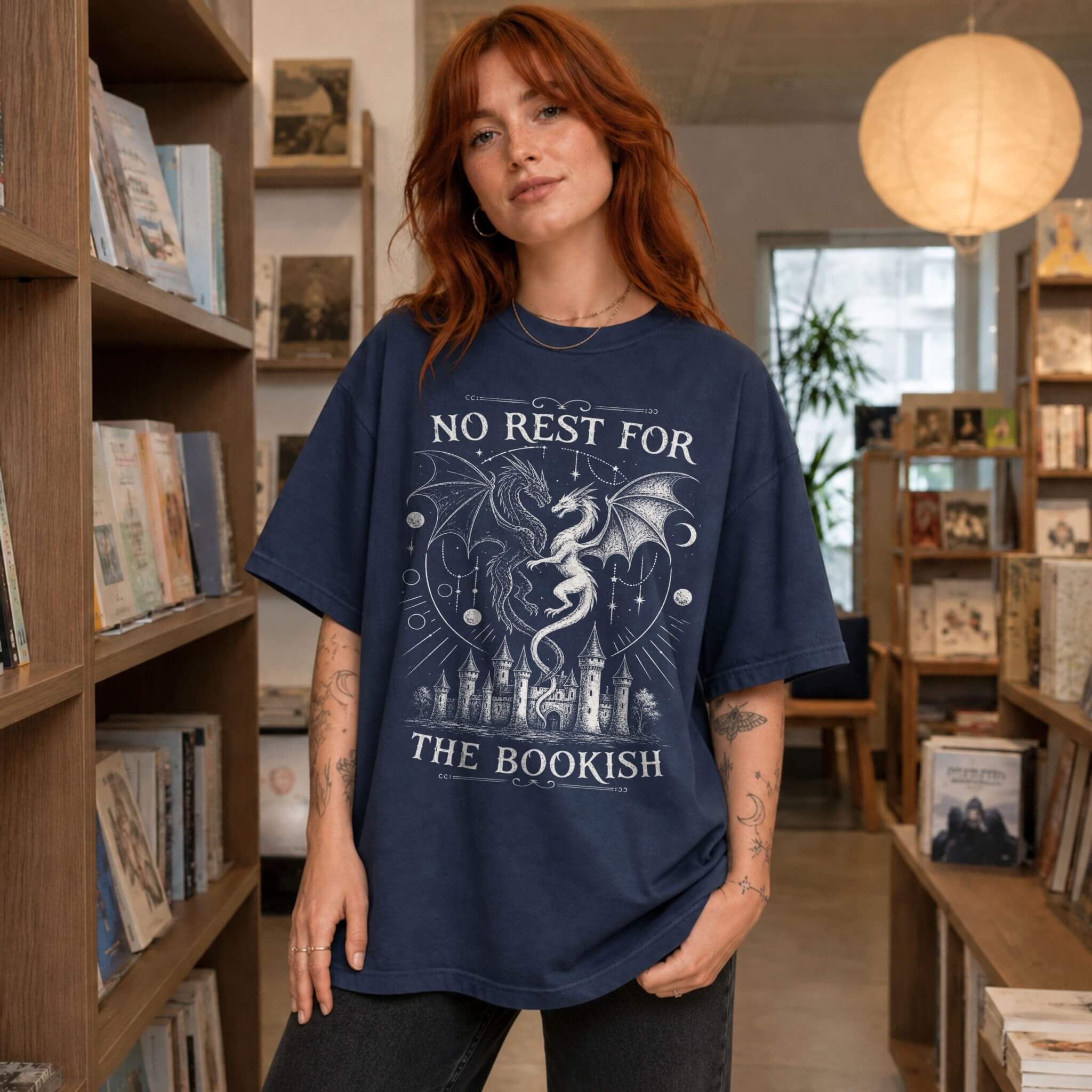 Navy color Comfort Colors 1717 relaxed fit t-shirt with gothic romantasy graphic — two dragons soaring over a castle beneath moons and celestial details, with the text "No Rest for the Bookish"