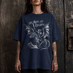 Woman wearing a navy color relaxed fit Comfort Colors tee with a vintage graphic of a woman warrior dragon rider and "We Ride at Dawn" text.