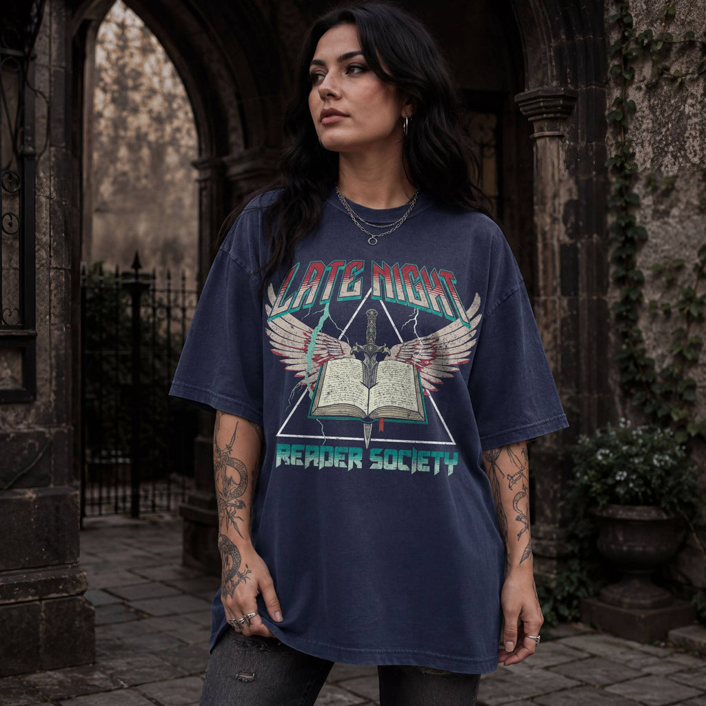 Woman wearing navy Comfort Colors relaxed tee with Late Night Reader Society vintage metal graphic — winged open book and dagger design
