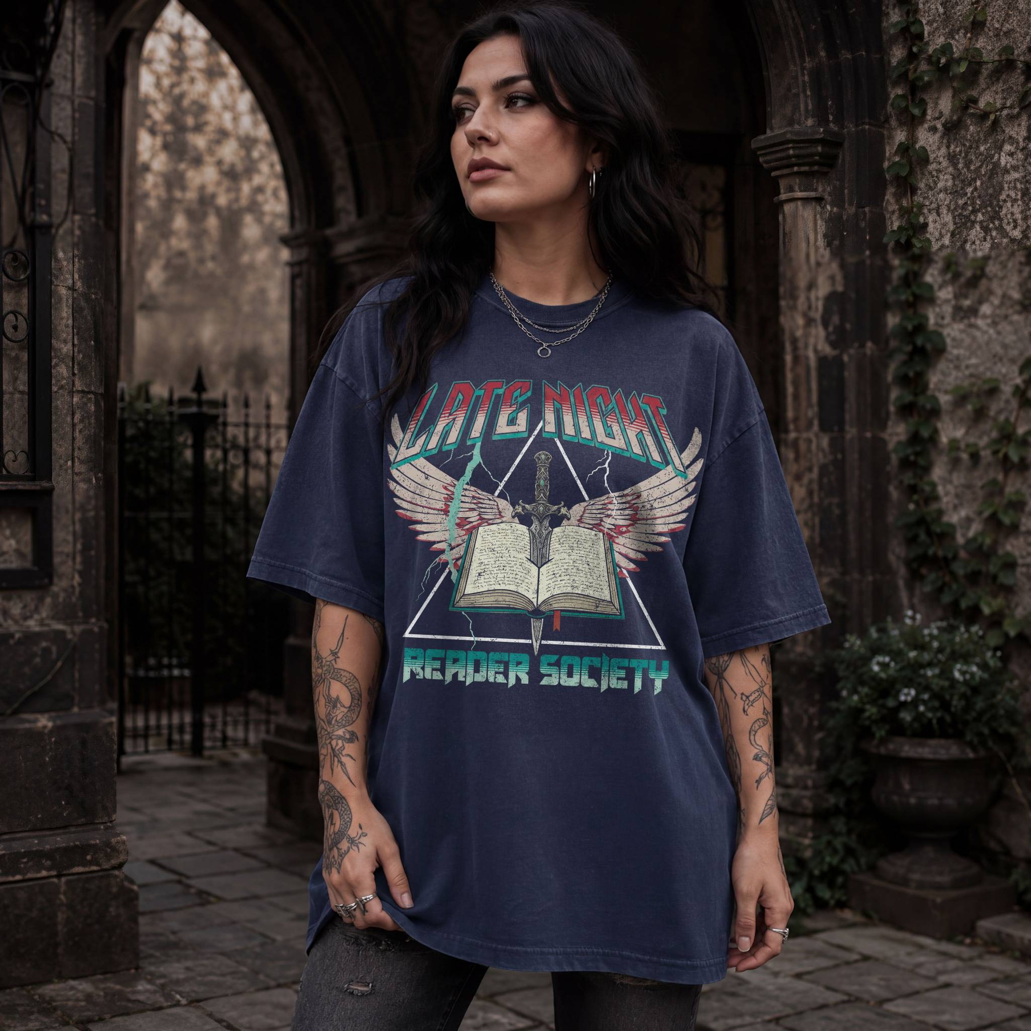 Woman wearing navy Comfort Colors relaxed tee with Late Night Reader Society vintage metal graphic — winged open book and dagger design