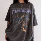 Woman wearing pepper Comfort Colors relaxed tee with Feminism vintage metal graphic — dragon and lava-flowing castle design