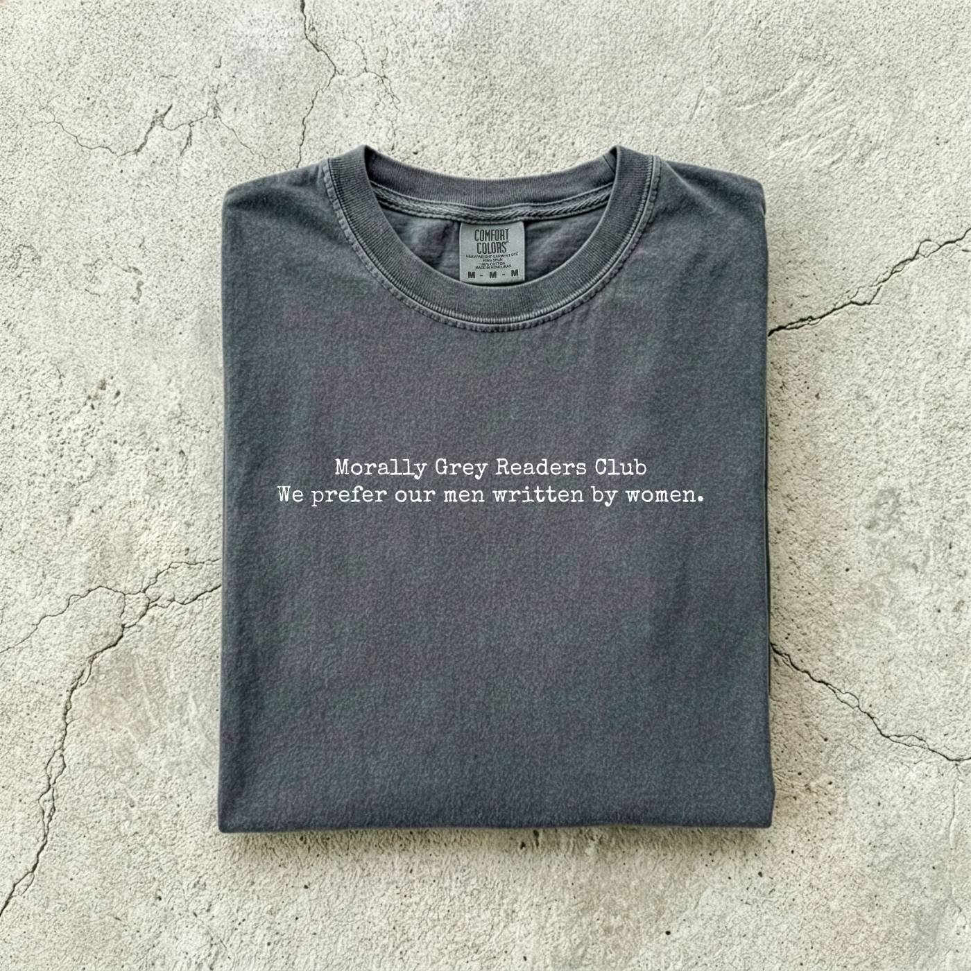 Pepper Comfort Colors tee folded flat on a concrete background reading "Morally grey readers club. We prefer our men written by women." in a minimal typewriter font.