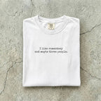White Comfort Colors tee folded flat reading "I like romantasy and maybe three people." in a typewriter font.