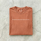 Yam Comfort Colors tee folded flat on a concrete background reading "Enemies make the best lovers." in a minimal typewriter font.