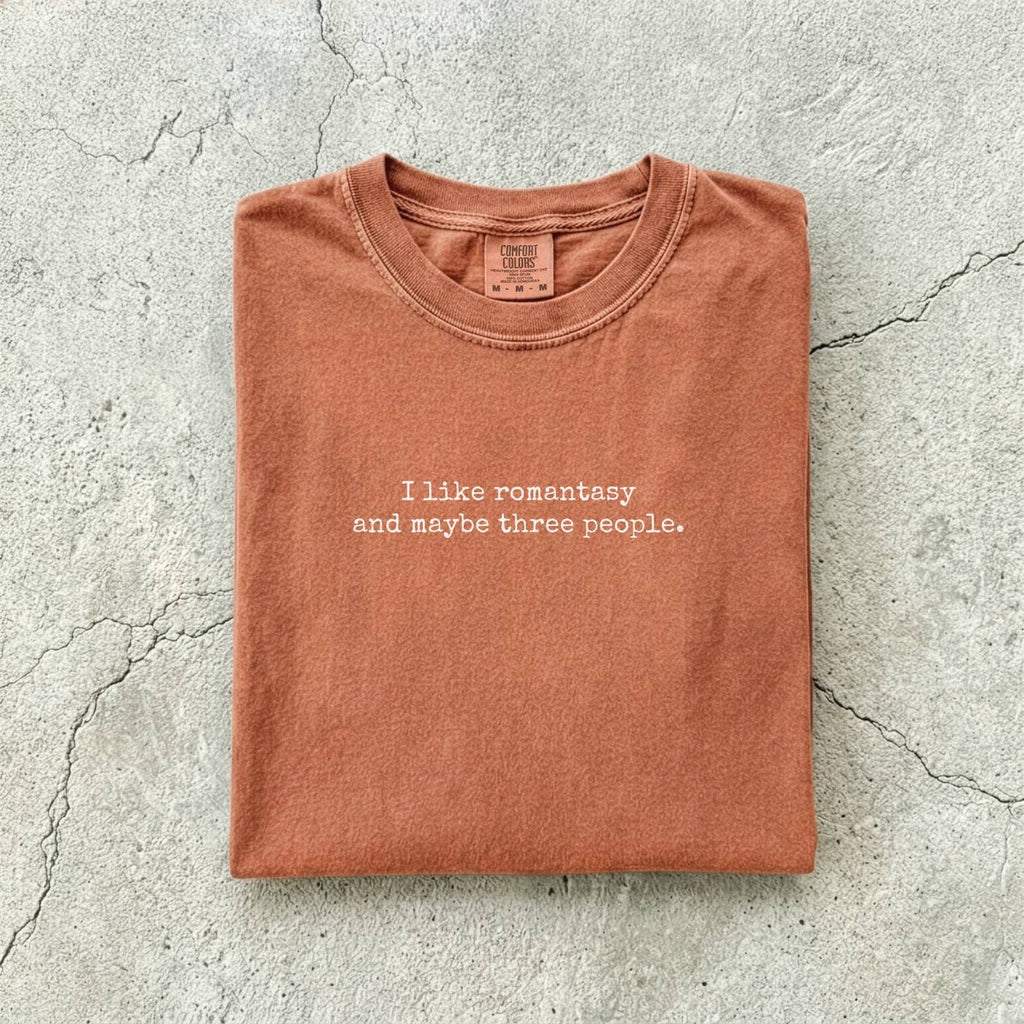 Yam Comfort Colors tee folded flat reading "I like romantasy and maybe three people." in a typewriter font.